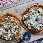Photo de pizzas maison préparées sur des pains naan, garnies de légumes colorés, fromage fondant, pesto et poulet grillé