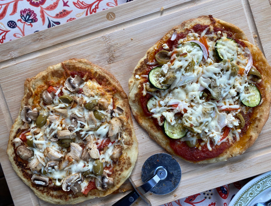 Photo de pizzas maison préparées sur des pains naan, garnies de légumes colorés, fromage fondant, pesto et poulet grillé