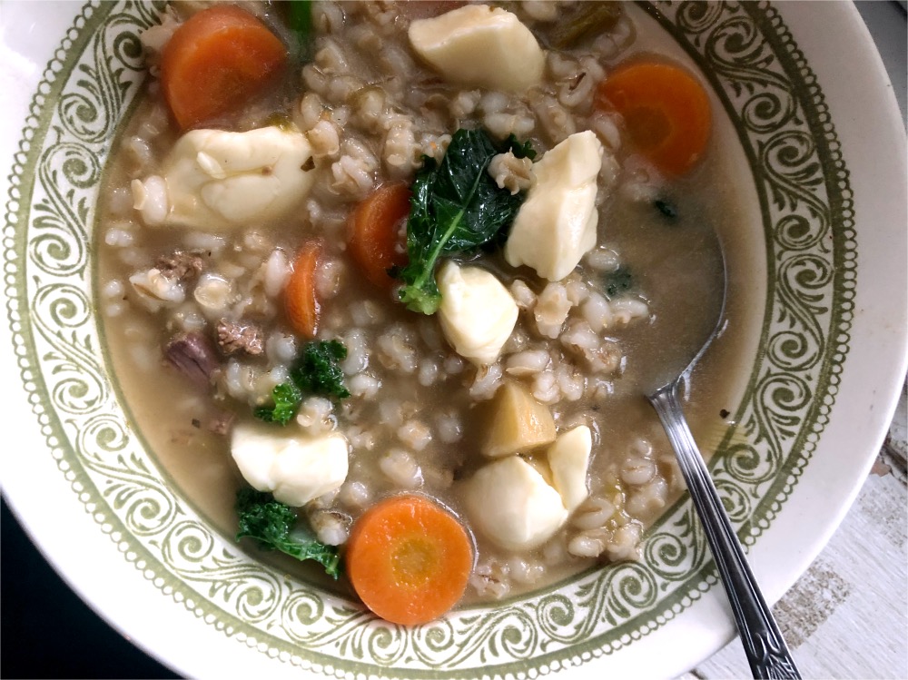 Bol de soupe chaude à l’orge, aux légumes racines, au bœuf et garni de fromage en grains fondant.