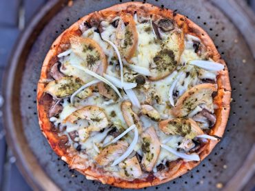 Pizza maison sur croûte de chou-fleur avec pesto, poulet grillé, légumes et fromage — une recette légère idéale pour la ménopause.