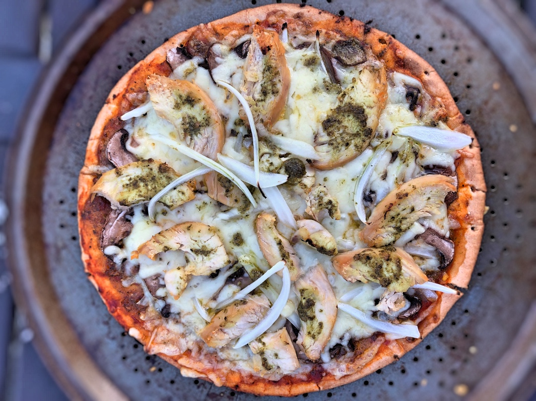 Pizza maison sur croûte de chou-fleur avec pesto, poulet grillé, légumes et fromage — une recette légère idéale pour la ménopause.